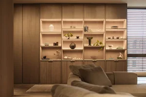A modern minimalist living room with wooden shelves displaying decorative items and books.