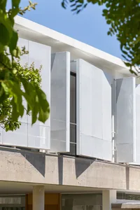 White perforated metal panels on a modern building facade under a clear blue sky.