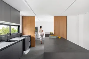 A modern minimalist kitchen with concrete countertops and wooden partitions, featuring a person in white attire.