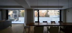 Modern residential dining room featuring a wooden dining table and glass walls overlooking a snowy courtyard.