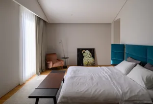 A minimalist bedroom with a blue velvet headboard, white bedding, and a textured wool floor.