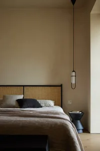 A minimalist bedroom with a wooden headboard and a bed with clean lines, accompanied by a hanging lamp and a bedside table.