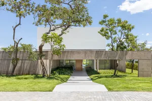 A modern, minimalist house with a concrete exterior features glass walls and a simple, straight path leading to the front doo
