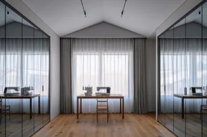 A minimalist workspace with wooden furniture, glass windows, and fabric curtains.