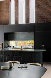 A modern kitchen with black wooden cabinetry, marble countertops, and large windows.
