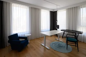 A modern home office with white curtains, wooden floors, and minimalist furniture.
