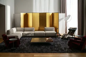A modern living room with a sectional sofa, gold metal wall divider, and dark flooring.