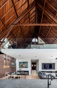 Modern living room with wooden accents, featuring a high ceiling with exposed beams and a cozy seating area.