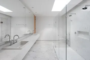 Modern bathroom interior with white marble finishes and glass shower enclosure.