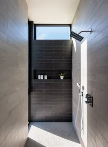 Modern minimalist bathroom with black tiles, white fixtures, and a window above the shower.