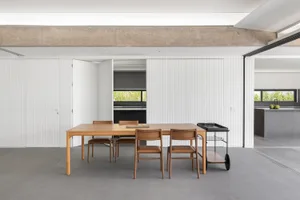 A modern minimalist kitchen with wooden table, brown chairs, and metal cart.