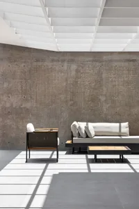 A modern minimalist living space featuring a concrete wall, wooden seating, and white cushions.