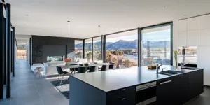 Modern kitchen featuring a large island with a metallic countertop, glass windows overlooking mountains, and a minimalist des