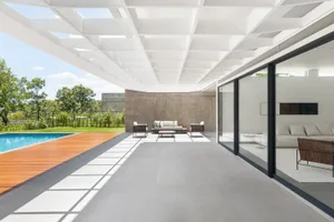 A modern outdoor patio featuring a concrete floor, glass walls, and wooden deck, with a minimalist design.