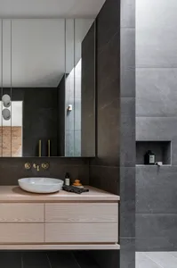 A modern bathroom with dark grey tiles, concrete sink, and brass faucet and wall.