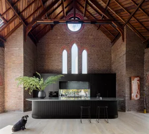 A modern farmhouse kitchen with a brick wall and concrete countertops featuring a white oak floor, black island, and black ba