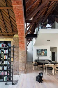 Modern residential space featuring exposed brick, concrete flooring, and wooden beams, with a black and white dog sitting on 