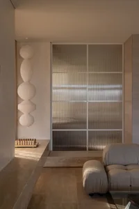 Minimalist living room featuring a frosted glass wall, beige sofa, and decorative lamps.
