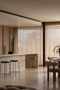 Modern residential kitchen featuring marble countertops, wooden furniture, and fabric-covered stools and chairs.