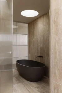 Modern bathroom featuring a concrete basin set against tiled walls, framed by a sleek glass partition.