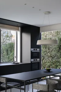 A modern black kitchen with dark wood features a large table and chairs, large windows, and a sleek, minimalist design.