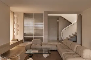 Modern living room with neutral tones, featuring a tufted sofa, glass coffee table, and decorative lighting.