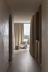 A minimalist living room with modern furniture and neutral tones, featuring a white chair and a view of the outdoors.