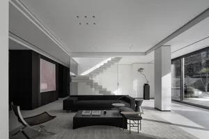 Modern minimalist living room with concrete walls, glass doors, and metal accents.