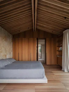A stylish minimalist bedroom with exposed wood beams and a rock wall.