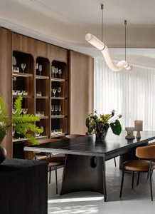 A modern dining room with a sleek black table, wooden shelves, and a contemporary chandelier.