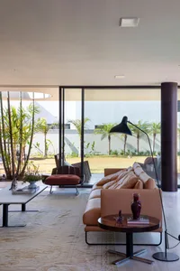 A modern living room featuring concrete and leather furniture, with a large window overlooking a tropical garden.