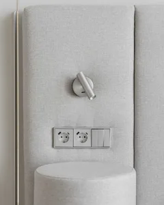 A modern interior wall featuring a light switch, power outlet, and light bulb installed on a neutral fabric wall panel.