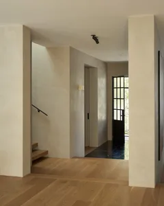 A modern minimalist entryway featuring light wood floors, concrete walls, and black metal accents.