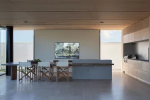 Modern residential kitchen featuring white dining chairs around a wooden dining table, a grey kitchen countertop, and a woode