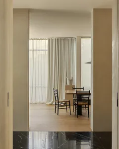 Minimalist dining room with wooden table and chairs, featuring sheer curtains and natural light.