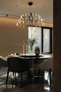 A modern dining room features a metallic round table, flowers, and a geometric chandelier.