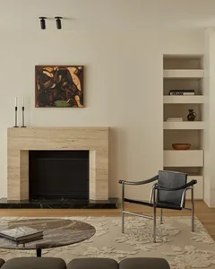 A minimalist living room features a marble fireplace and coffee table, a black leather armchair, and a round marble coffee ta