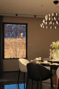 A modern dining room featuring minimalist furniture, a round table with a minimalist chandelier, and a large window overlooki