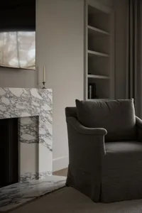 A modern lounge area featuring a marble fireplace and upholstered armchair.