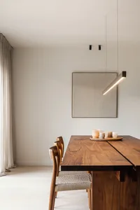 A minimalist dining room featuring a wooden table with a hanging lamp and candles.