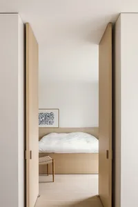 A spacious minimalist bedroom with white walls, a comfortable bed, and wooden furniture.