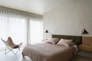 A minimalist bedroom with grey walls, black blinds, and a grey floor.
