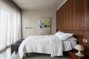 Minimalist bedroom with a white bed and wooden walls. The room features simple, clean lines and a serene atmosphere.