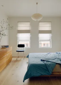 A minimalist bedroom featuring a wooden floor, a blue bedspread, and a black chair.