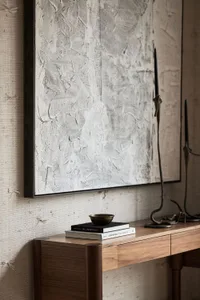 A minimalist console table with a wooden surface, topped with two books, a bronze bowl, and an abstract black and white paint