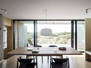 A modern minimalist dining room featuring a wooden table, black chairs, and a large window overlooking a natural landscape.
