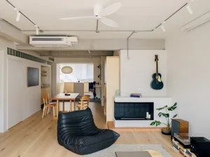 Modern minimalist living room featuring brick and concrete walls, a black leather beanbag chair, a white rug, and a guitar on