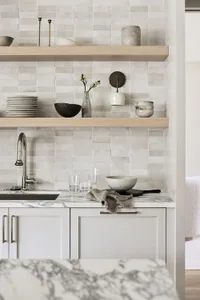 Minimalist kitchen with white cabinets, wooden shelves, ceramic tiles, and marble countertop.
