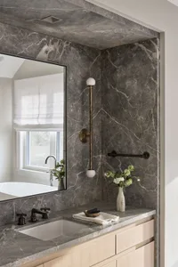 A modern marble bathroom featuring a sink with a faucet, a mirror, and a decorative vase with flowers.