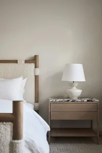A modern, minimalist bedroom featuring a bed with a wooden headboard, marble accents, and a textured blanket.